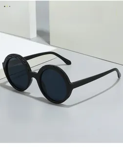 Detail of round sunglasses with textured black frames and dark grey lenses on white cube