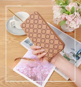 Close-up of a long brown patterned wallet with a gold zipper held by a model