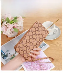 Close-up of a compact brown monogram zipper wallet held in hand with lifestyle decor
