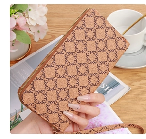 Close-up of a brown monogram zip wallet with a wristlet held over a wooden table