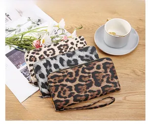 Three leopard print long wallets with gold zippers on a wooden table with accessories