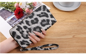Detailed view of leopard print clutch wallet with gold zipper and wrist strap on a table