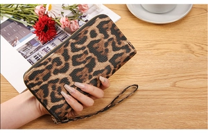 Detail of leopard print long wallet for women with wrist strap on a wooden desk