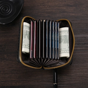 Classic black accordion leather card holder with gold zipper on a wooden desk