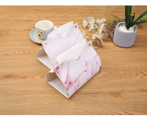 Pink marble textured leather tissue box holder with gold snaps on a wooden tabletop