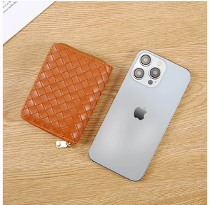 Orange woven leather card holder next to a smartphone for size comparison on wood background