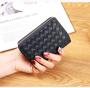 Detail of woven texture wallet with gold metal zipper held by hand over wooden desk