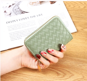 Handheld pale green woven leather wallet with gold zipper on a wooden desk background