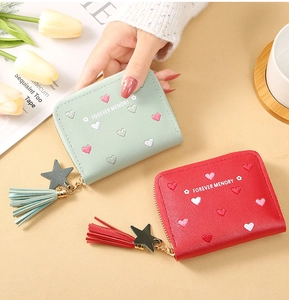 Detail of short leather wallets with heart embroidery and tassel star charms in soft colors