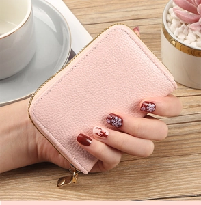 Pink lychee grain leather card holder with gold zipper detail held by manicured hand