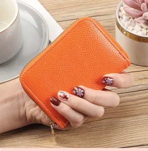 Close-up of bright orange lychee grain leather card holder with gold zipper detail