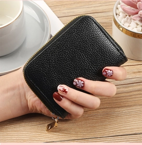 Close-up of black lychee grain leather card holder with gold zipper held by hand