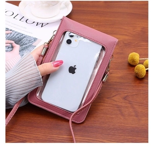 Detail of pink crossbody phone bag with touch screen window on a wooden table