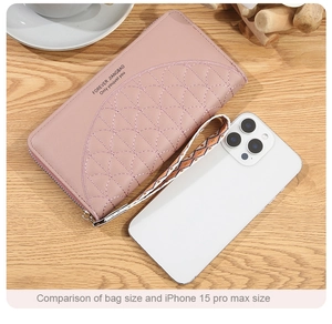 Pink long PU leather wallet size comparison with iPhone 15 Pro Max on wood desk