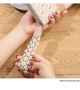 Close-up of beige long wallet with patterned motifs and a wide geometric wrist strap