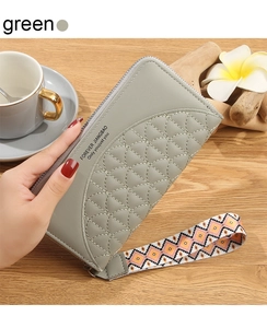 Detail view of a long green quilted wallet with a patterned wrist strap on a wooden desk