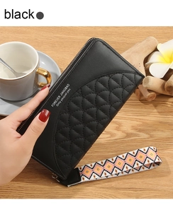 Detail of black long quilted wallet with patterned wristlet strap on a desk