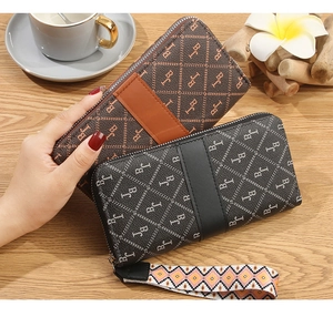Close-up of long zip-around wallets with monogram print and woven wristlet straps