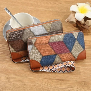 Women's long patchwork wallet with geometric block patterns and wrist strap on wood desk