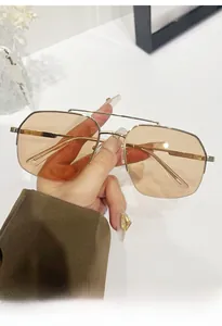 Detailed view of pilot sunglasses with gold metal frame and amber lenses held by hand