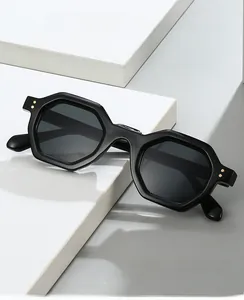 Detail of black hexagonal sunglasses with golden rivet accents on white geometric stand