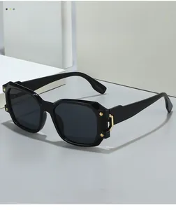 Dettaglio di occhiali da sole neri oversize con borchie geometriche in metallo dorato sulle aste