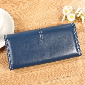 Détail d'un long portefeuille en cuir bleu foncé avec surpiqûres blanches sur bois