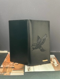 Detail of black pebbled leather wallet featuring an embossed eagle and metal logo