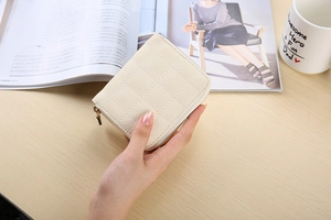 Close-up of beige quilted mini wallet with zipper held by hand on wooden desk