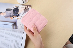 Close-up of pink quilted leather mini wallet with zipper held over a wooden desk