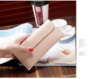 Detailed texture of pink litchi pattern long wallet for women held in hand over a desk