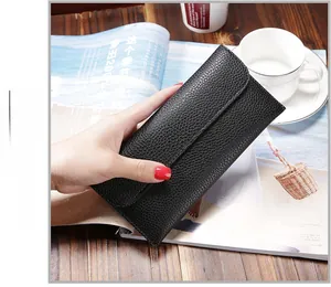 Minimalist black pebble grain leather long envelope wallet held over a wooden table