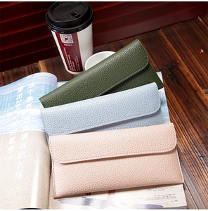 Close-up of litchi texture leather wallets in green blue and pink on a wooden desk