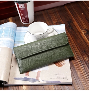 Deep green long leather wallet with lychee pattern on a rustic wooden desk with coffee