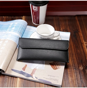 Detailed view of black litchi grain long wallet on a desk with coffee and magazines