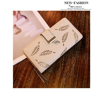 Détail du portefeuille beige avec motif de feuilles découpées et pendentif doré