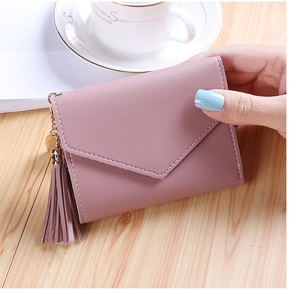 Detailed macro view of the litchi grain texture and tassel charm on pink trifold wallet