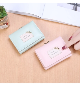 Detail view of light green and pink tri-fold wallets with pearls on wooden surface