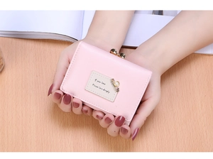Close-up of pink tri-fold faux leather wallet with pearl charm and lettered patch