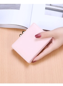 Close-up of pink PU leather tri-fold short wallet with gold metal clasp on wooden table