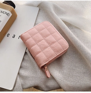 Close-up of pink quilted mini wallet with golden zipper on a soft fabric background