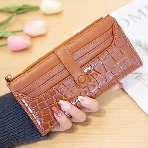 Brown long wallet with crocodile texture held over a wooden table with soft lighting