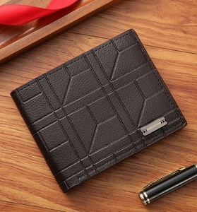 Detail of dark brown leather wallet with geometric pattern and metallic logo on wood surface