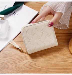 Petit portefeuille matelassé beige avec pompon tenu au-dessus d'un bureau élégant