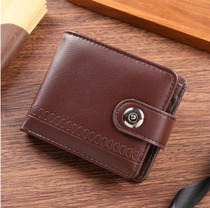 Detail view of a brown pebbled leather bifold wallet with snap button on a wooden desk