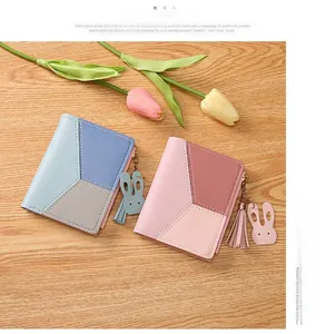 Detail of bicolored PU leather wallets with rabbit charms and tassel zippers on wood