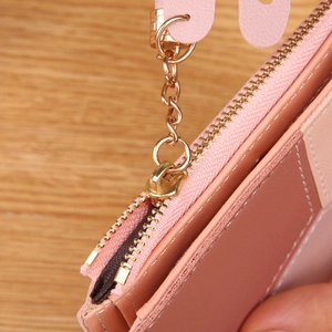 Pink patchwork faux leather wallet with golden zipper and heart tassel on wooden desk