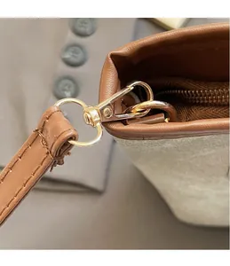 Details der goldenen Metallhaken und braunen Lederriemen an einer beigen Handtasche