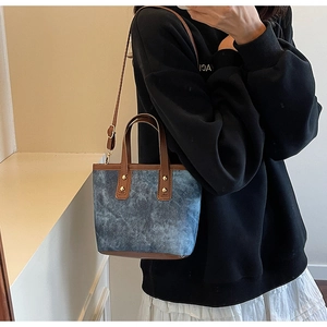 Detail of blue denim shoulder bag with brown leather trim and metallic studs on model