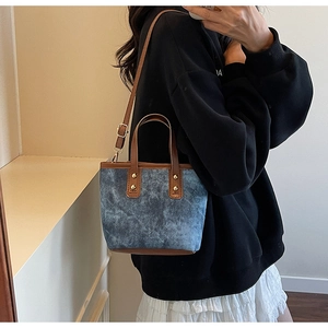Détail du mini cabas en denim bleu avec anses en cuir marron et rivets dorés